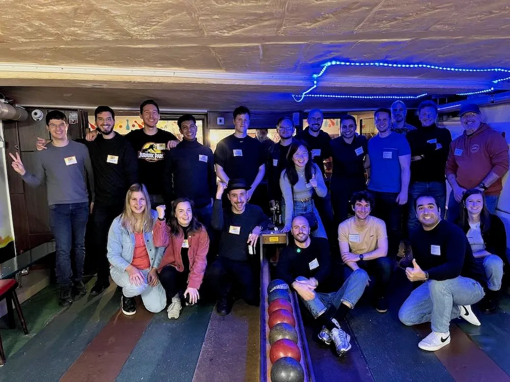 Group of about 20 people posing at a bowling alley with colorful bowling balls on the lane