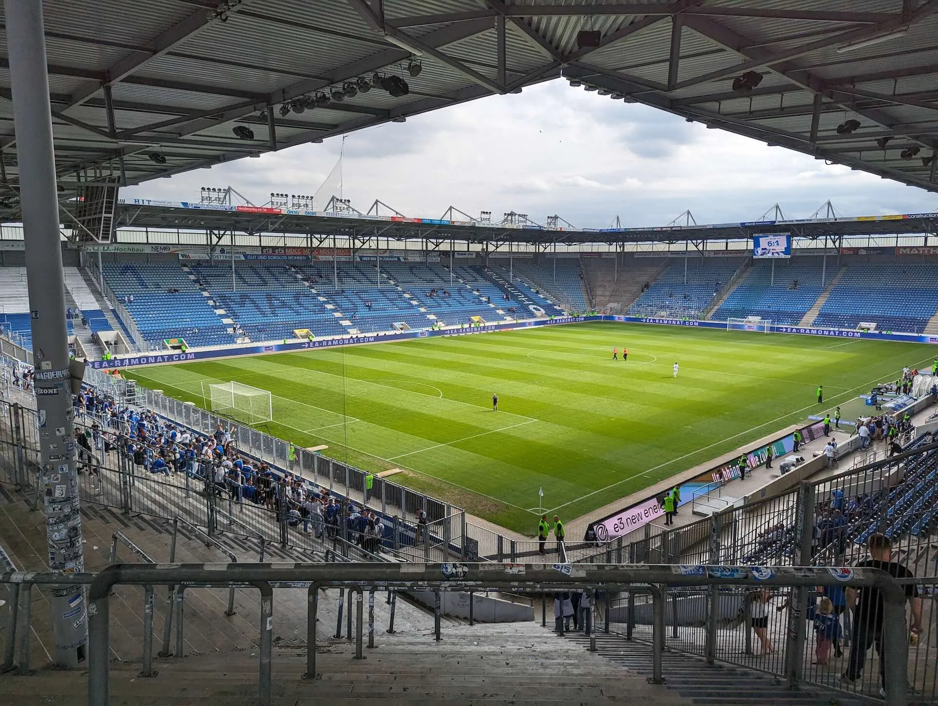 Interior of 1. FC Magdeburg's MDCC-Arena showing the pitch, blue seating, and main stand from an upper tier